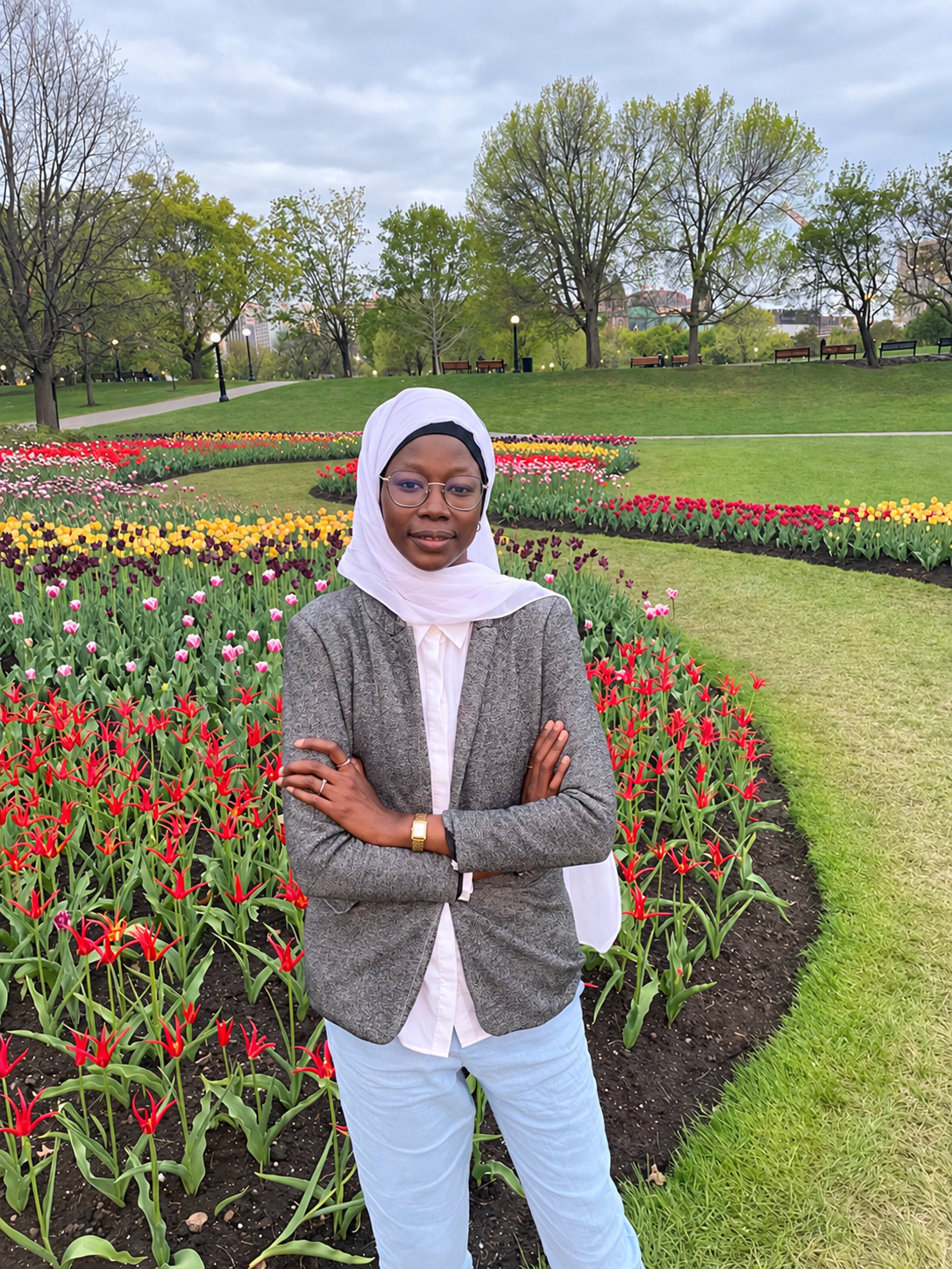 Dr. Awa Diop in a white hijab and grey blazer, standing in a flower garden.